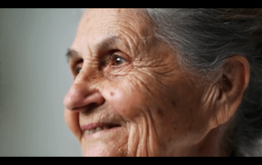 Screenshot of AI video close-up of Caucasian elderly woman with brown eyes smiling